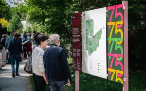 Koppel van middelbare leeftijd kijkend naar infobord aan hoofdingang kunstpark met op de achtergrond een aantal bezoekers